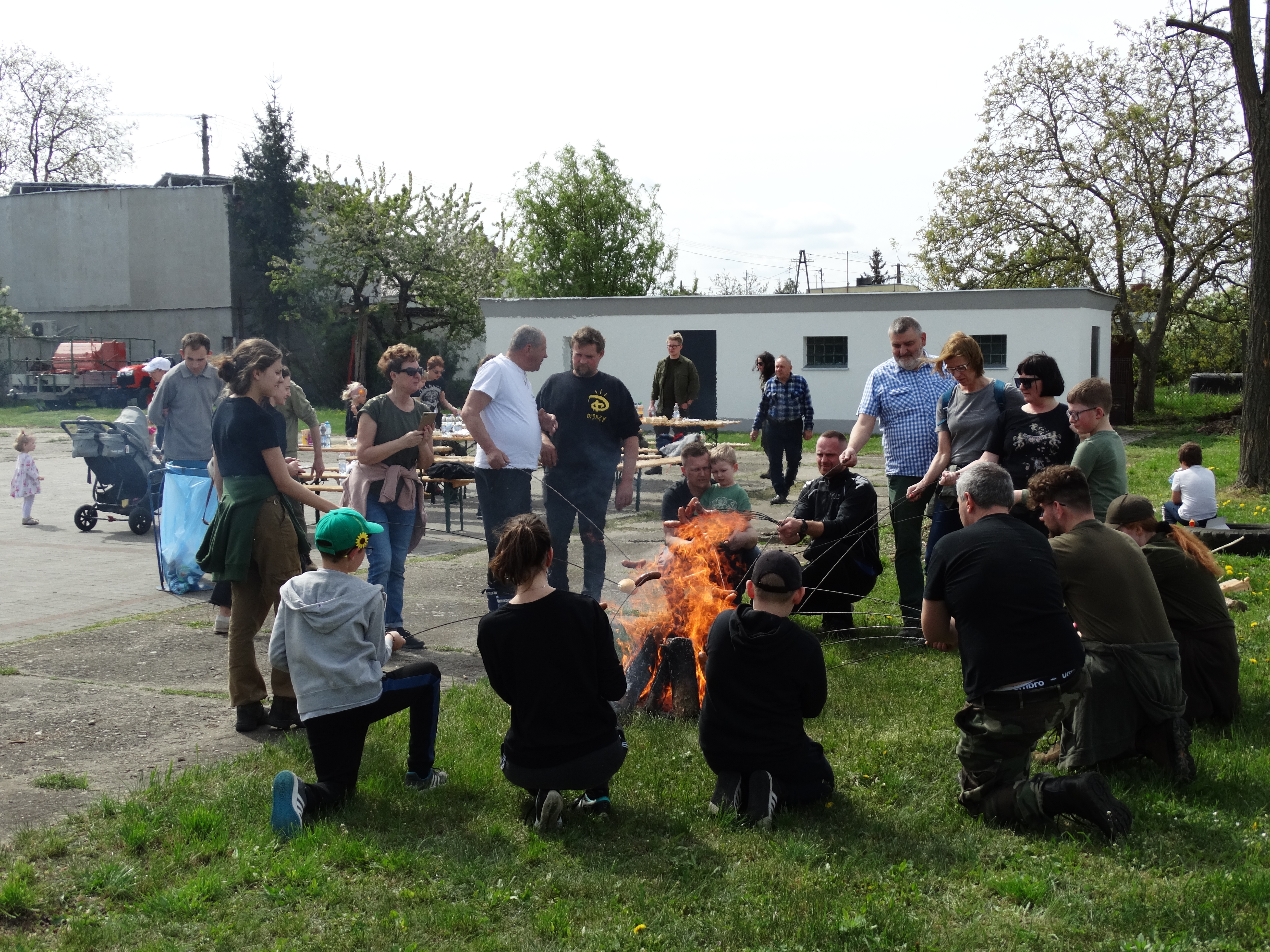 Zdjęcie przedstawia uczestników akcji pieczących kiełbasy przy ognisku.